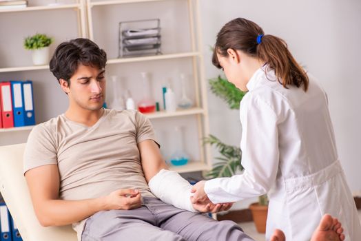 Young man with bandaged arm visiting female doctor traumatologist