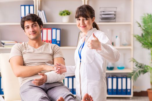 Young man with bandaged arm visiting female doctor traumatologist