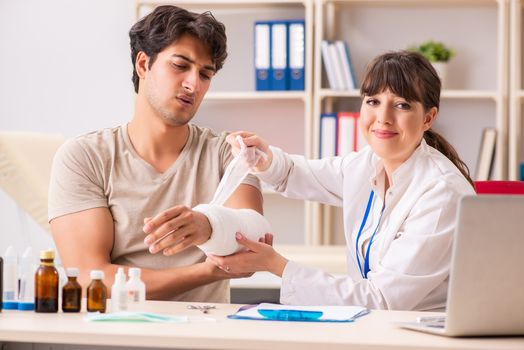 Young man with bandaged arm visiting female doctor traumatologist