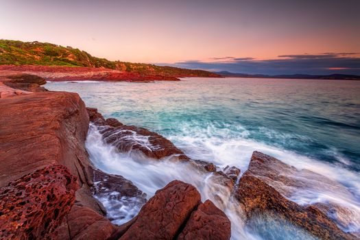 Early morning coastal burquoise waves over the rich red rocks of Eden Australia