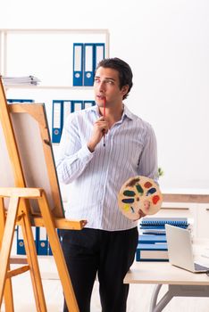 Young handsome employee enjoying painting at the office 