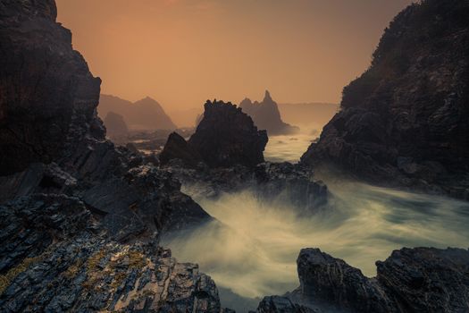 Mystical sea fog, sea spray and sunrise on the sharp craggy volcanic rock coastline 