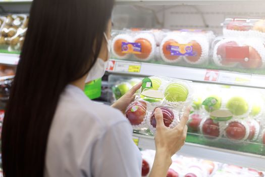Women long hair wear protective face mask hands holding green and red apples ipackage. Asian female shopping at supermarket, Grocery to buy some food. New normal after covid-19 concept.