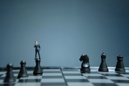 Business strategy conceptual photo - miniature businessman standing above castle pawn on a chessboard