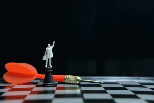 Business strategy conceptual photo - miniature businessman standing above castle pawn on a chessboard with red arrow