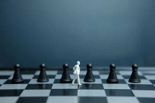 Miniature of businessman walking above black pawn on a chessboard. image photo