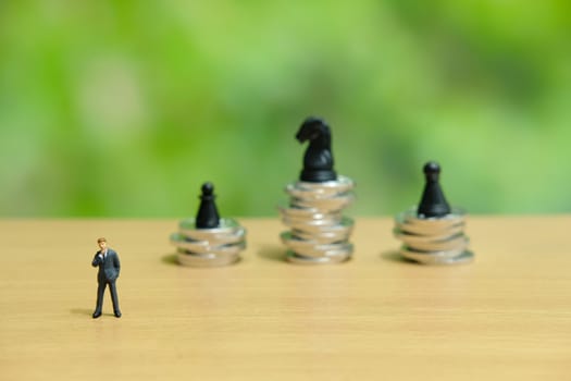 Business strategy conceptual photo - miniature businessman in front of coin stack with chess pawn on top of it