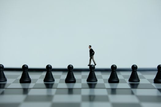 Business strategy conceptual photo - Miniature of businessman walking above black pawn on a chessboard