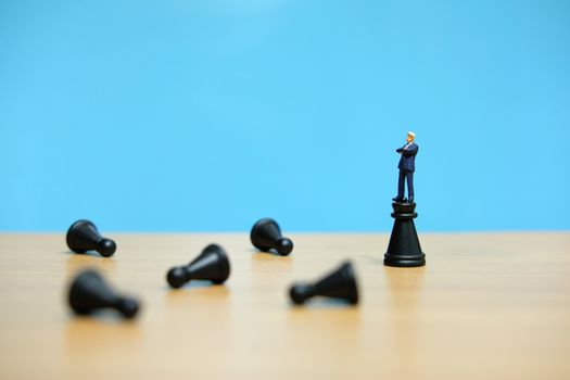 Business strategy conceptual photo - miniature businessman standing on castle chess piece in between falling chess piece