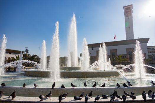 Casablanca Morocco Place Mohammed V fountain 12/31/2019 water spouts and pigeons. Photographed against the sun light to give the water fountains glowing white High quality photo