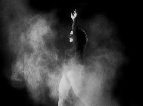 beautiful caucasian woman in a black bodysuit with a sports figure is dancing in a white cloud of flour on a black background, black white toning
