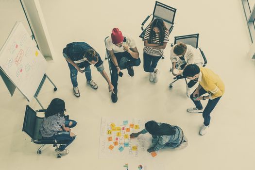 Top view Group Of Asian and diverse Business people with casual suit brainstorming and helping to put postit paper on the project chart together in the modern workplace, multiethnic teamwork concept