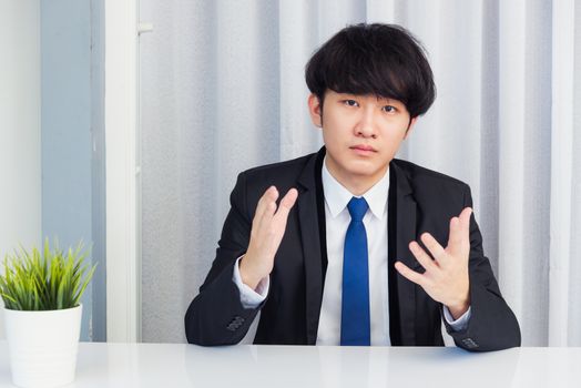 Work from home, Close up face of Asian young businessman video conference call or facetime he looking to camera raises hands to explain about his job to team on a desk at the home office