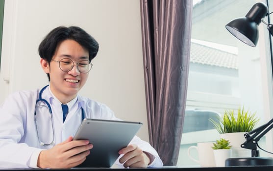 Happy Asian young doctor handsome man smile work from home office wear glasses, using black modern smart digital tablet computer on desk at hospital office, Technology healthcare and medicine concept