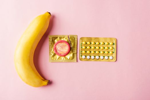 World sexual health or Aids day, Top view flat lay condom on wrapper pack, banana and contraceptive pill, studio shot isolated on a pink background, Safe sex and reproductive health concept