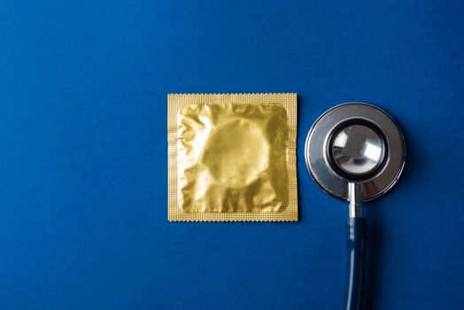 World sexual health or Aids day, Top view flat lay medical equipment, condom in pack and stethoscope, studio shot isolated on dark blue background, Safe sex and reproductive health concept