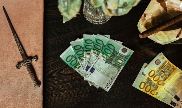 Hundred euro bills laid on a plush table with cigar and dagger. Still life euro with table.