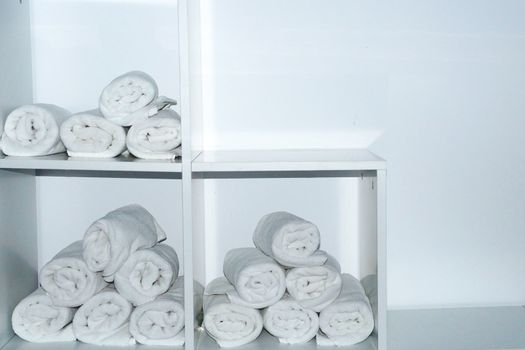 rolled white towels on white shelves close up