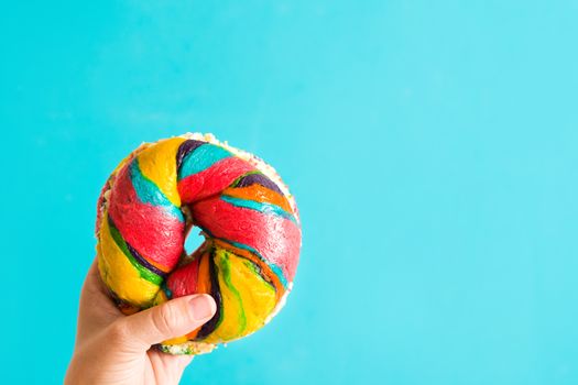 Colorful bagel with cheese and sprinkles in hand on blue background