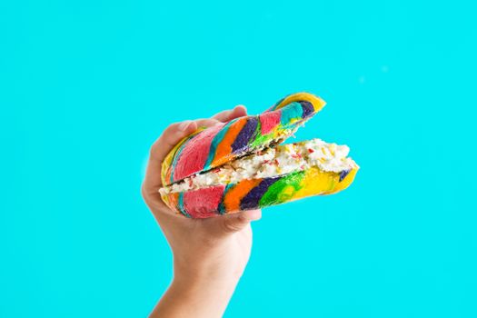 Colorful bagel with cheese and sprinkles in hand on blue background