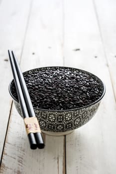 Raw black rice on white wooden background