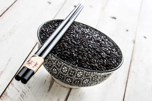 Raw black rice on white wooden background