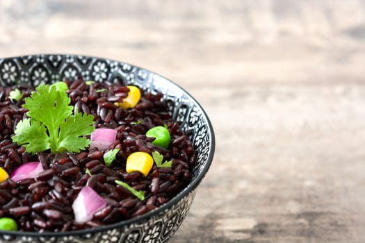 Black rice in a bowl and vegetables on wooden table