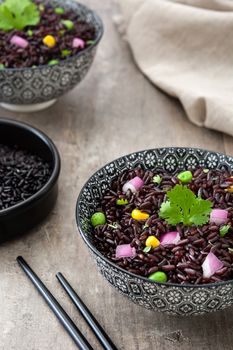 Black rice in a bowl and vegetables on wooden table