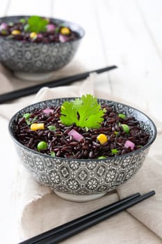 Black rice in a bowl and vegetables on wooden table