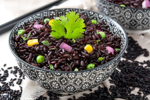 Black rice in a bowl and vegetables on wooden table