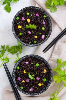 Black rice in a bowl and vegetables on white marble