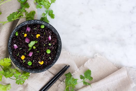 Black rice in a bowl and vegetables on wooden table