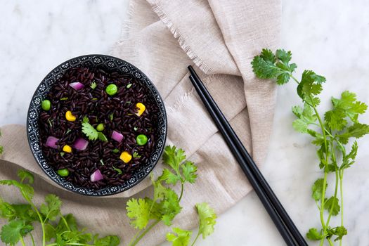 Black rice in a bowl and vegetables on white marble