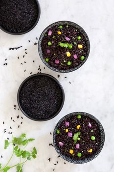 Black rice in a bowl and vegetables on white marble