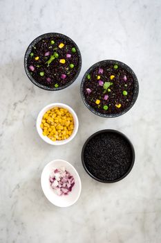 Black rice in a bowl and vegetables on white marble