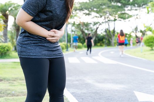 Asian woman suffering from stomach ache while running at the park. Injury from sport and exercise concept.