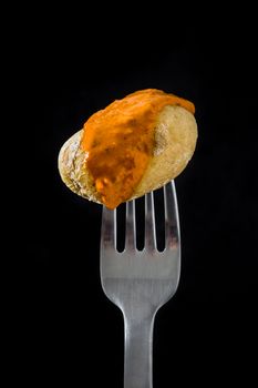 Canarian potato (papa arrugada) with mojo sauce on a fork with black background