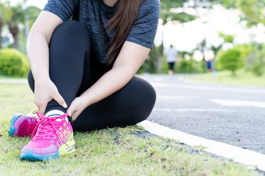 Asian woman use hands hold on her ankle while running on road in the park. Injury from workout concept.
