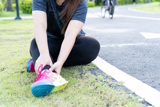 Asian woman use hands hold on her ankle while running on road in the park. Injury from workout concept.