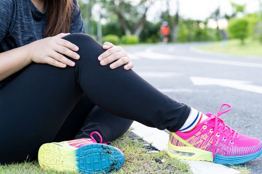 Asian woman use hands hold on her knee injury while running on road in the park, Injury from workout concept.