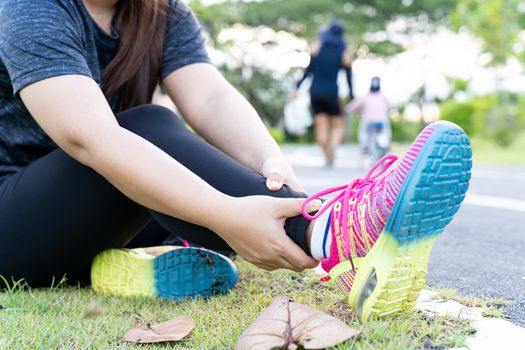 Asian woman use hands hold on her ankle while running on road in the park. Injury from workout concept.