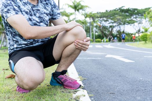 Asian man use hands hold on his knee injury while running on road in the park, Injury from workout concept.