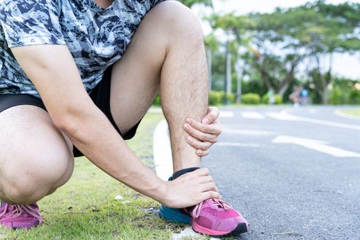 Asian man use hands hold on his ankle while running on road in the park. Injury from workout concept.