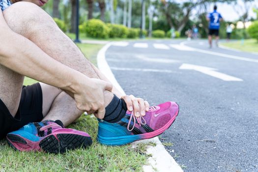 Asian man use hands hold on his ankle while running on road in the park. Injury from workout concept.
