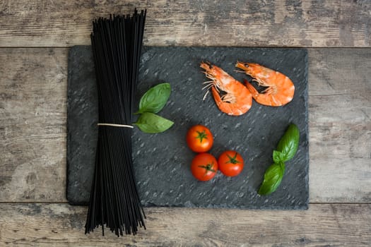 Raw black spaghetti with prawns, tomatoes and basil on wooden background