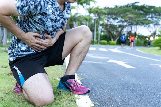 Asian man suffering from stomach ache while running at the park. Injury from sport and exercise concept.