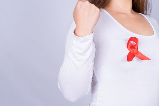 Red AIDS awareness ribbon on woman chest and raise her hand to fight them on grey background. World Aids Day, Healthcare and medical concept.