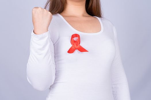 Red AIDS awareness ribbon on woman chest and raise her hand to fight them on grey background. World Aids Day, Healthcare and medical concept.
