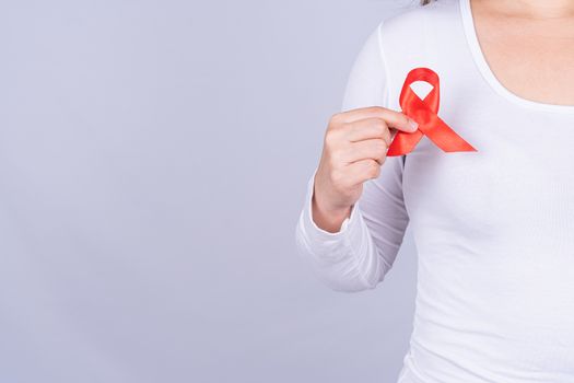 Red AIDS awareness ribbon on woman chest and raise her hand to fight them on grey background. World Aids Day, Healthcare and medical concept.