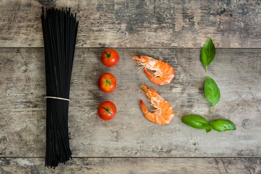 Raw black spaghetti with prawns, tomatoes and basil on wooden background